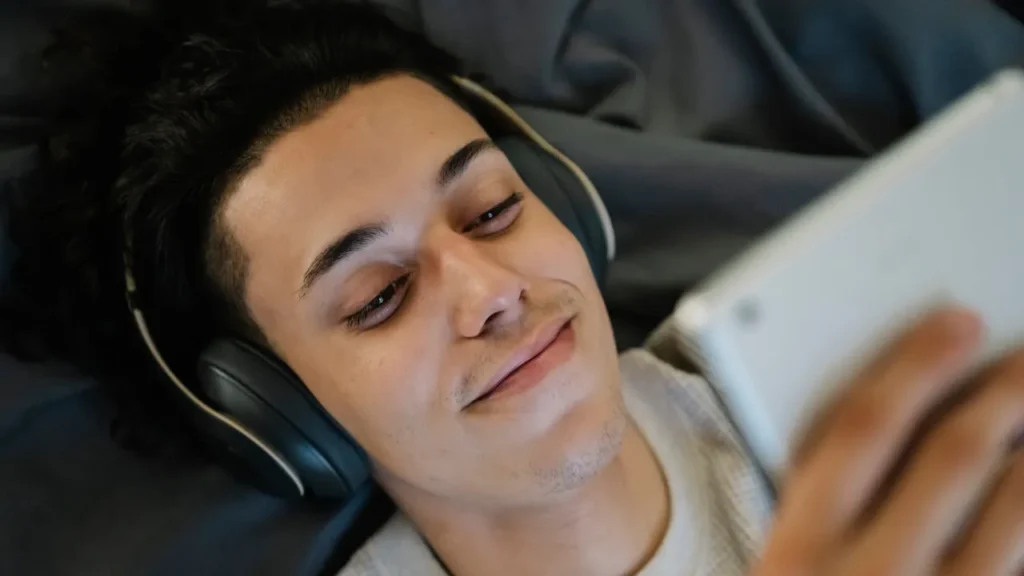 Photo of man listening to music while lying down and looking at tablet