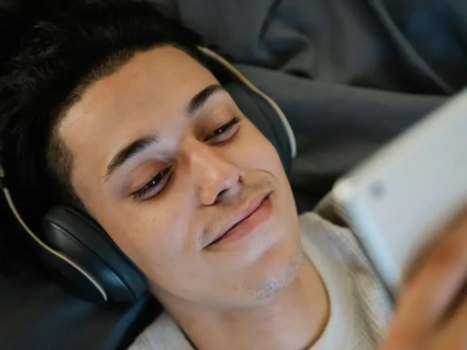 Photo of man listening to music while lying down and looking at tablet